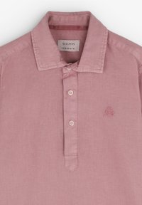 Lyserød polo T-shirt lavet af blødt stof, med en knaplukning, spids krave og broderet kranie-logo over venstre bryst.