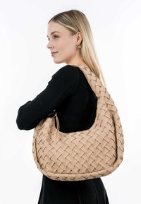 Braided beige tote bag made of soft material with a rounded shape; features a wide shoulder strap and no external hardware.