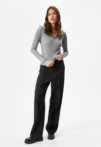 Maglione grigio a coste con maniche lunghe e colletto con zip, abbinato a pantaloni neri a vita alta e gamba larga e scarpe nere chunky.