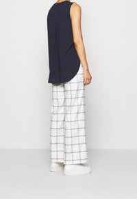 Marineblauw mouwloos shirt met een ronde zoom, gecombineerd met witte geblokte broek met blauwe accenten. Glad stoftextuur, ontspannen pasvorm.