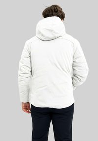 Giacca bianca con cappuccio, con una texture trapuntata e cuciture rinforzate, vista da dietro. Abbinata a pantaloni scuri.