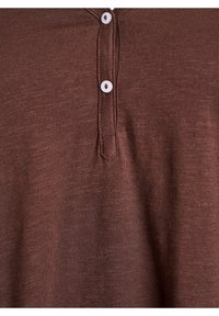 Rjava henley majica z teksturirano tkanino. Ima kratek preklop z dvema belima gumboma in subtilnim meliranim vzorcem po celotni površini.