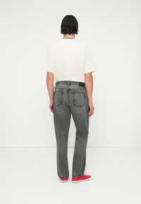 Pantalon en denim gris avec une coupe décontractée, présentant une texture légèrement délavée, associé à une chemise de couleur claire et des baskets rouges.