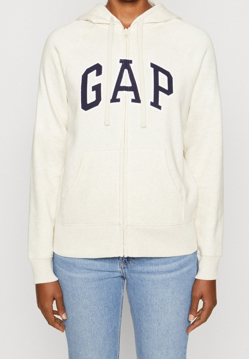 Sweat à zip crème avec logo "GAP" bleu marine, poches kangourou, capuche à cordon de serrage et poignets côtelés. Fabriqué à partir d'un matériau doux et texturé.
