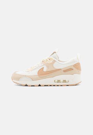 Baskets Nike Air Max blanches et beiges avec amorti à air visible, fermeture lacets à l'avant et logo Swoosh sur le côté, sur un fond uni.