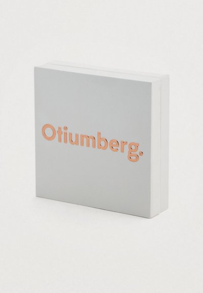 Γκρι ορθογώνιο κουτί με απαλή υφή, που διαθέτει ανάγλυφο λογότυπο «Otiumberg.» σε χάλκινο χρώμα στο εμπρόσθιο μέρος.