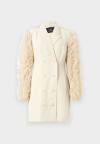Blazer double boutonné couleur crème avec des manches en chiffon beige froncées. Présente de grands boutons et une coupe ajustée. Design simple et élégant.