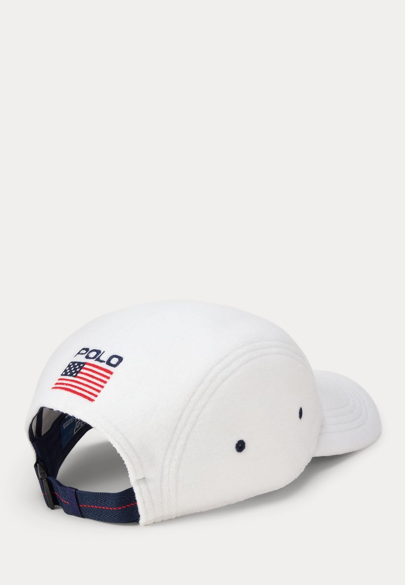 Vit fleecemössa med böjd skärm, prydd med "POLO" i marinblått och en amerikansk flaggemblem. Justerbar marinblå rem med röda sömmar.