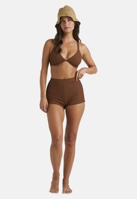 Braunes, geripptes Bikini-Set mit einem dreieckigen Oberteil und einer hochgeschnittenen Unterhose. Model trägt einen geflochtenen Strohhut.