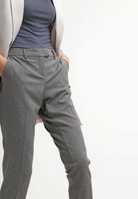 Grå rutiga byxor med rak skärning, med sidfickor och slät framsida. Tygets struktur är slät med subtila mönster.