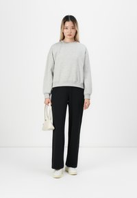 Grå sweatshirt med rund hals och ribbad mudd, kombinerad med svarta skräddarsydda byxor. Modellen håller en liten vit handväska. Vita sneakers fulländar looken.