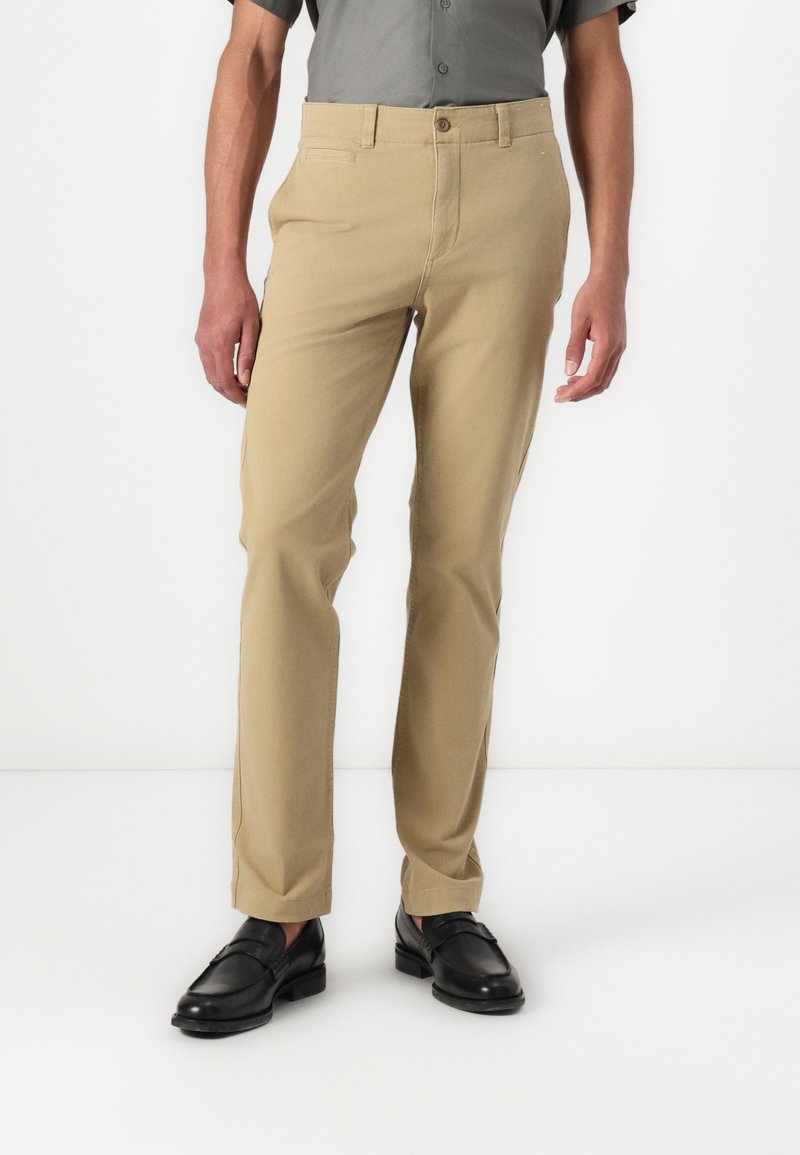 Beige chinos made of cotton blend fabric. Features a straight leg design, front pockets, and a button closure at the waist.