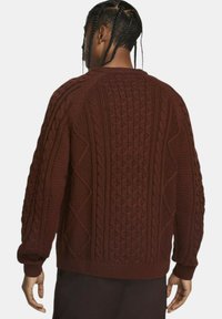 Brun kabelstrik sweater med forskellige teksturerede mønstre, ribbede ærmekanter og kant, samt en afslappet pasform. Udsigten viser bagsidedesignet.