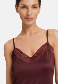 Camisola bordeaux con scollatura in pizzo e spalline sottili, realizzata in morbido tessuto di raso con una texture liscia.