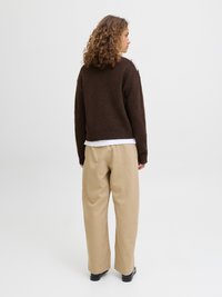 Sweater de malha castanho com um corte largo e bainha canelada, combinado com calças largas de tom bege claro, usadas com sapatos pretos.