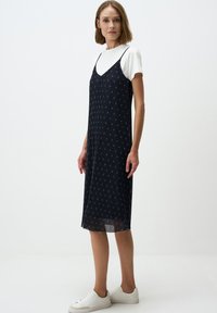 Navy spaghetti strap jurk met een slim fit en bloemmotief; gelaagd over een witte t-shirt met korte mouwen en gecombineerd met witte sneakers.