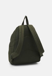 Mochila verde con correas de malla acolchada y una superficie texturizada. El diseño es moderno, con una forma distintiva y sutiles acentos de hardware.