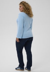 Pull bleu clair en tricot à manches longues avec ourlet côtelé, associé à un jean foncé et des chaussures de sport bleues avec des rayures blanches.