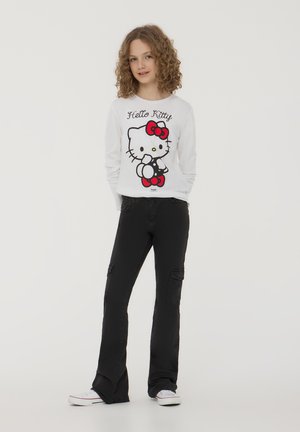 Camicia bianca a maniche lunghe con una grafica colorata di Hello Kitty, abbinata a pantaloni cargo neri a palazzo e sneakers bianche.