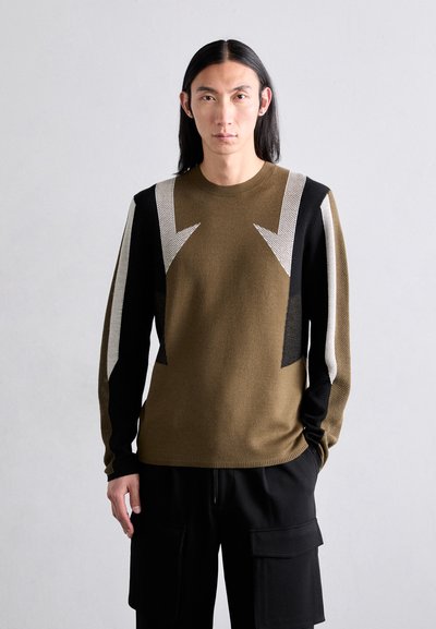 Strickpullover in Olivgrün mit auffälligen schwarz-weißen geometrischen Mustern auf den Schultern. Lange Ärmel, runder Ausschnitt, weiche Textur.