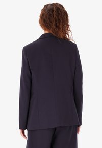 Blazer navy realizzato in tessuto testurizzato, con colletto classico e vestibilità su misura con pince posteriori per una silhouette affusolata.