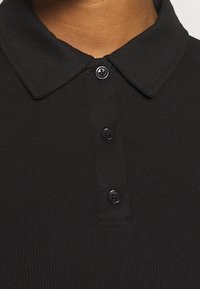 Schwarzes geripptes Polo-Shirt mit umgeschlagenem Kragen, ausgestattet mit drei schwarzen Knöpfen entlang der Knopfleiste und einem strukturierten Stofffinish.