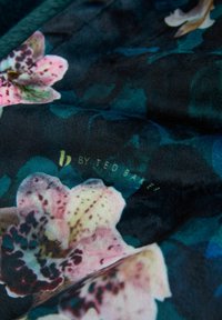 Floral fabric featuring pink orchids on a dark green background, smooth texture, with "b by Ted Baker" printed in gold.