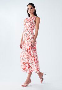 Mouwloze midi-jurk in een koraal- en witte bloemenprint, met een aangesloten lijfje en een vloeiende rok. Aangevuld met een decoratief schouderdetail.