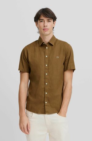 Brown short-sleeve shirt with a button-up front, featuring light green buttons and a small logo on the chest. Worn with light-colored pants.