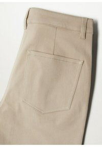 Pantalon beige avec une poche plaquée arrière, des passants de ceinture et des surpiqûres visibles sur un fond blanc.