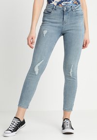 Jeans ajustados celestes con detalles desgatados. Hechos de denim con una textura suave y un diseño de alta cintura. Combinados con zapatillas negras.