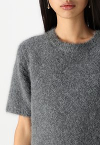 Maglione grigio in lana a maniche corte con una consistenza soffice, scollatura rotonda e vestibilità rilassata, caratterizzato da dettagli di design minimalisti.