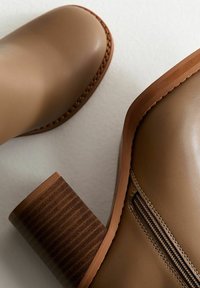 Brązowe skórzane botki za kostkę z masywnymi, podwyższonymi obcasami i bocznymi zamkami błyskawicznymi, ukazane z góry w zbliżeniu na jasnym tle.