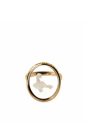 Anillo de oro con una piedra preciosa clara y circular que presenta un ave blanca grabada con las alas extendidas dentro de la piedra.