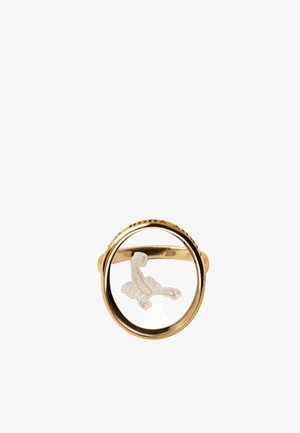 Anillo de oro con una piedra preciosa clara y circular que presenta un ave blanca grabada con las alas extendidas dentro de la piedra.