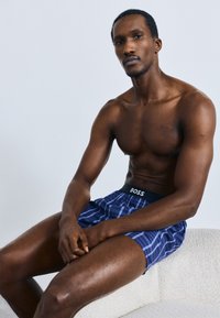 Temno modri karo bokserji s črnim elastičnim pasom z napisom "BOSS". Gladek material, sproščen kroj in dolžina do sredine stegna.