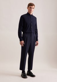 Camicia a maniche lunghe blu navy con colletto a punta, abbinata a pantaloni sartoriali a vita alta e scarpe con lacci nere. Tessuto liscio, vestibilità strutturata.