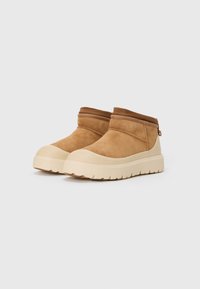 Bruine suède enkellaarsjes met een gepadded kraag en een beige rubberen zool, met tekstuurelementen aan de zijkanten en een ritsluiting.