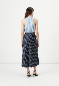Maxikjole med lyseblå halterneck og en marineblå nederdel med hvide prikker. Glat stof med en løs pasform, ankel-længde design.