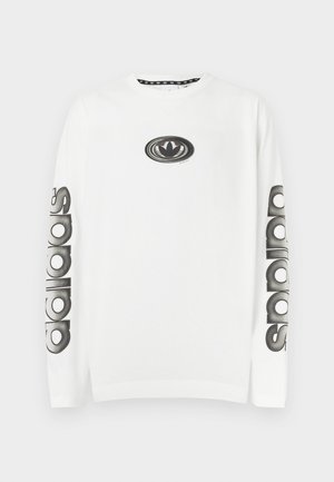 Valkoinen pitkähihaisen collegepaita, jossa on musta logografiikka rinnassa ja "adidas"-teksti painettuna hihoihin kohokuvioidulla fontilla.