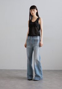 Top negru fără mâneci cu bretele subțiri, combinat cu blugi evazați de culoare albastră deschis, cu buzunare la spate și o ușoară decolorare. Design simplu, croială modernă.