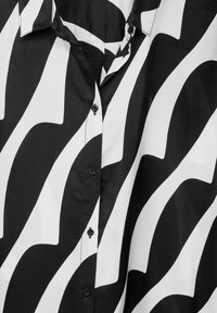 Camicia button-up bianca e nera con motivo a onde, texture setosa, colletto a punta e bottoni neri lungo la patta.