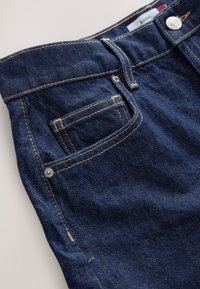 Ciemnoniebieskie dżinsy z gładką fakturą, z kontrastującym przeszyciem, przednią kieszenią i metalowym guzikiem na pasku talii.