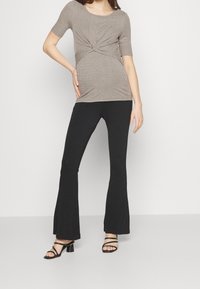 Ribbad, taupe topp med knutdesign framtill, ihop med svarta utsvängda byxor och svarta sandaletter, vilket skapar en avslappnad silhuett.