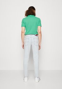 Camisa polo verde combinada con jeans de mezclilla azul claro. La camisa tiene mangas cortas y un cuello clásico; los jeans tienen un ajuste relajado y un diseño minimalista.