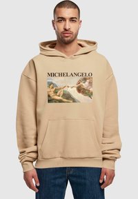 Beige Kapuzenpullover mit einer Fronttasche und einem grafischen Druck von Michelangelos Kunstwerk, mit dem Namen "MICHELANGELO" über dem Bild.
