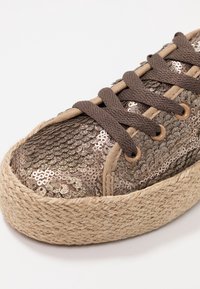 Baskets recouvertes de sequins en bronze avec des lacets marron et une semelle en jute tissée. Bout arrondi et dessus texturé. Présente deux œillets de chaque côté.