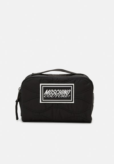 Găleată cosmetică neagră, capitonată, cu formă rectangulară, fermoar superior și un patch alb cu logo-ul Moschino Couture pe față.