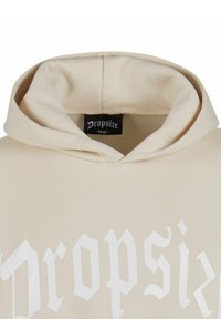 Beige Kapuzenpullover mit großem weißen Aufdruck "Dropsize". Verfügt über eine verstellbare Kapuze und eine weiche, glatte Stofftextur.