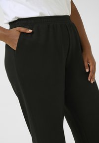 Pantalon de survêtement noir en tissu doux, avec une taille élastique, des poches latérales et une texture lisse.